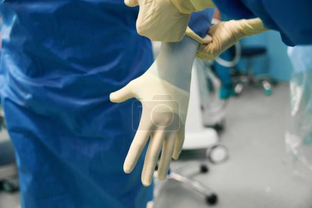 Téléchargez les photos : Le chirurgien est mis sur des gants stériles avant l'opération, il est assisté par un assistant - en image libre de droit