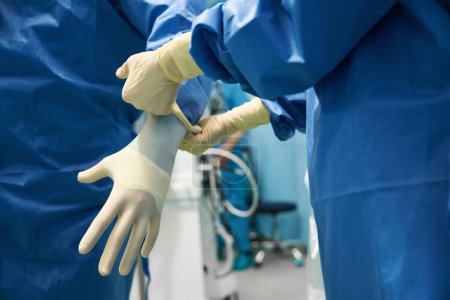 Téléchargez les photos : Médecin est mis sur des gants stériles avant l'opération chirurgicale, un assistant l'aide - en image libre de droit