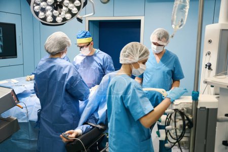 Photo for Surgical team performs an operation in a sterile operating room, the patient has a heart rate monitor on his finger - Royalty Free Image