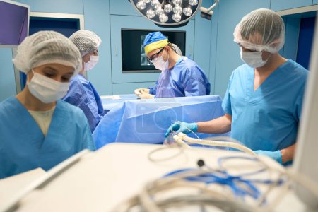 Foto de Anestesiólogo entrega medicamentos al paciente a través de una máscara, todos los miembros del equipo quirúrgico trabajan sin problemas - Imagen libre de derechos