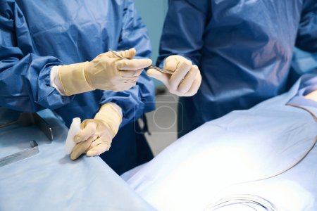 Foto de La gente se para en la mesa de operaciones en el quirófano, tienen un instrumento quirúrgico en sus manos - Imagen libre de derechos