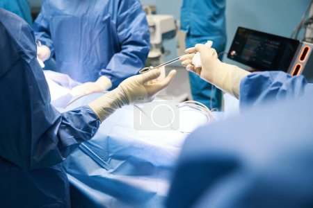 Photo for Man in operating room passing surgical instrument to colleague, people in surgical uniform - Royalty Free Image