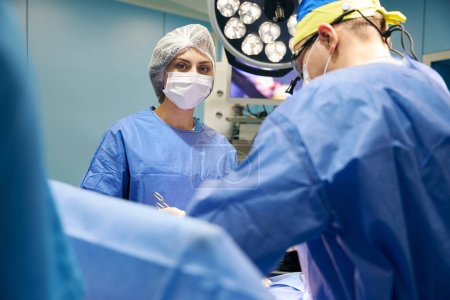 Photo pour Assistante féminine tient un clip chirurgical dans ses mains, le chirurgien travaille avec une caméra spéciale - image libre de droit