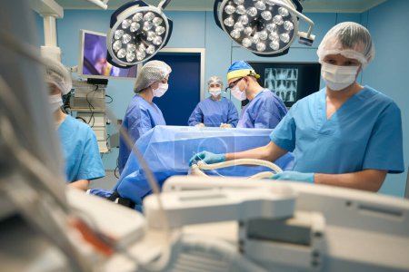 Photo for Anesthesiologist at work in a modern operating room, nearby his fellow surgeons are doing their part of the work - Royalty Free Image