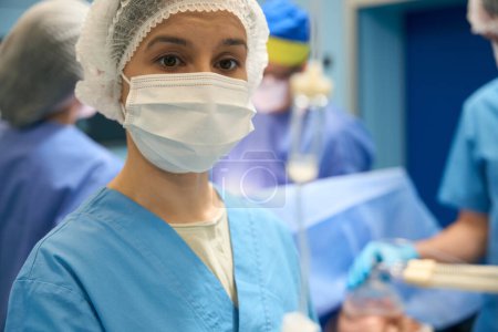 Foto de Mujer asistente en el trabajo en quirófano, en el fondo de la mesa de operaciones, cirujanos y anestesióloga - Imagen libre de derechos