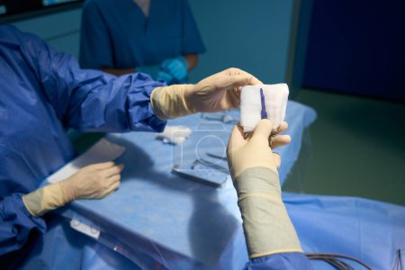 Téléchargez les photos : L'assistante dans la salle d'opération passe le scalpel au chirurgien, les gens en uniforme chirurgical - en image libre de droit