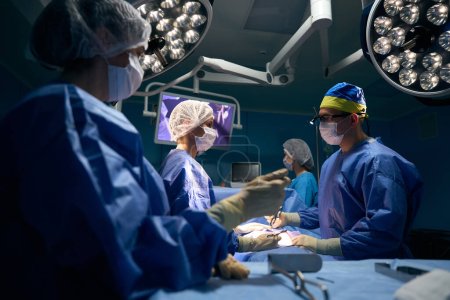 Téléchargez les photos : Une équipe de médecins opère un patient dans une salle d'opération moderne, le patient sous anesthésie repose sur la table - en image libre de droit