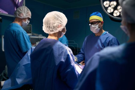 Téléchargez les photos : Chirurgien, anesthésiste et assistants travaillent à la table d'opération, le patient s'allonge sur la table sous anesthésie - en image libre de droit