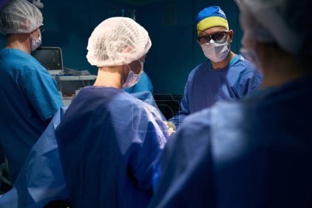 Foto de Anestesiólogo, enfermera operadora, cirujano y asistentes trabajan en la mesa de operaciones, el paciente se acuesta en la mesa bajo anestesia - Imagen libre de derechos