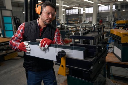 Foto de Hombre con guantes protectores y auriculares instalando estructura metálica en la máquina en la fábrica - Imagen libre de derechos