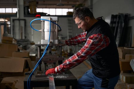 Téléchargez les photos : Masculin dans des lunettes de protection et des gants utilisant un cylindre pneumatique pour traiter les détails en acier dans l'atelier - en image libre de droit