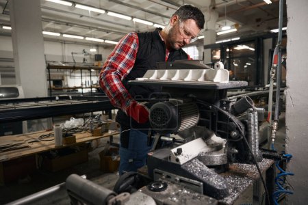 Téléchargez les photos : Homme en vêtements de protection et gants de travail sur machine de découpe dans l'atelier - en image libre de droit