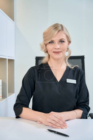 Foto de Retrato de una bonita cosmetóloga con abrigo médico sentada en la oficina y lista para trabajar - Imagen libre de derechos