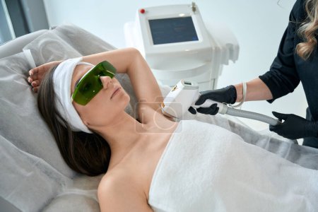 Photo for Beautician in protective gloves standing near young female and doing laser hair removal on armpit - Royalty Free Image