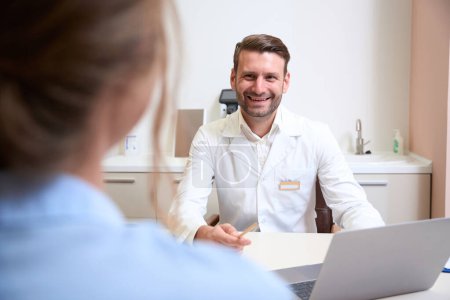 Photo for Waist up portrait of laughing handsome doctor is working with patient in medical office - Royalty Free Image