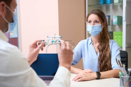 Photo for Waist up portrait of charming lady in protective mask is listening advise of professional doctor in medicine center - Royalty Free Image