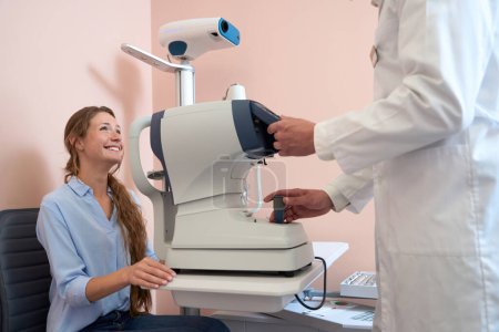 Photo for Waist up side view portrait of charming smiling female patient is talking with doctor in ophthalmology clinic - Royalty Free Image