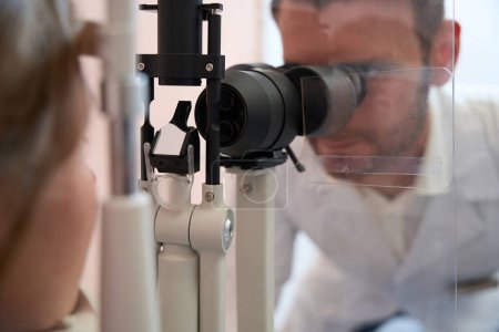 Téléchargez les photos : Gros plan portrait du médecin examine la vue avec un dispositif spécial dans la clinique opticien - en image libre de droit