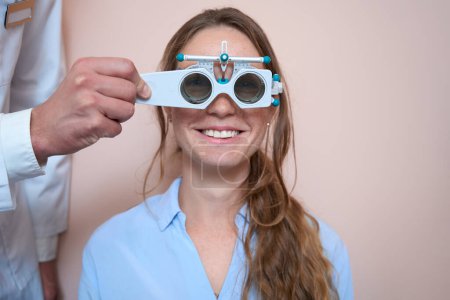 Téléchargez les photos : Vue de face portrait de la femme caucasienne riante visite l'optométriste tout en vérifiant son acuité visuelle dans le centre médical - en image libre de droit