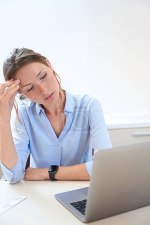 Foto de Primer plano retrato de encantadora un poco cansada mujer está sentado en el escritorio y mirando a la pantalla de la computadora en su oficina - Imagen libre de derechos