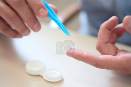 Photo for Close up picture of man hands is holding contact lenses with tweezer above the table - Royalty Free Image