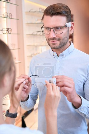 Foto de Retrato de vista frontal de hombre eficaz adorable está recibiendo consultoría para comprar gafas de estilo moderno en la tienda de óptica - Imagen libre de derechos