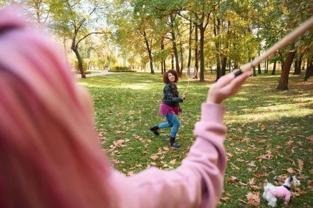 Téléchargez les photos : Joyeuse jeune femme avec raquette à la main traversant la pelouse en présence d'un autre joueur - en image libre de droit