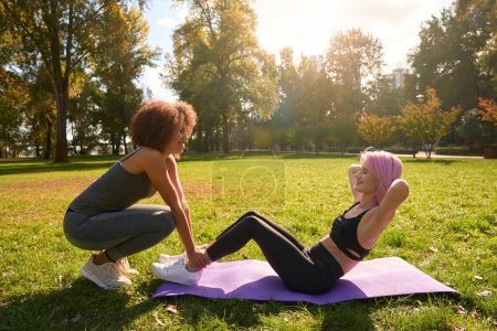 Photo for Smiling sporty woman doing crunches on yoga mat assisted by her fitness partner - Royalty Free Image