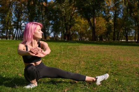 Photo for Fit young Caucasian woman performing side lunge on lawn in public park - Royalty Free Image