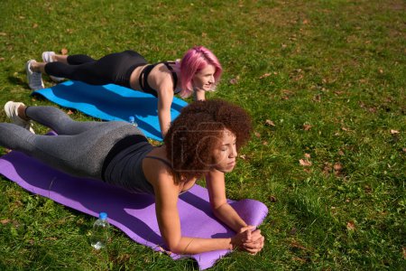 Photo for Serious sporty woman and her joyous fitness partner performing forearm plank in public park - Royalty Free Image
