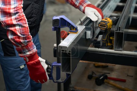 Foto de Masculino en guantes protectores ajuste abrazadera para fijar el detalle de acero en la mesa en el taller - Imagen libre de derechos