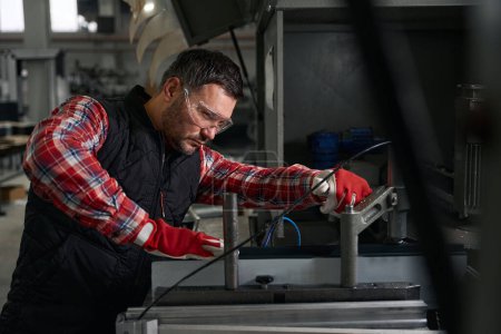 Téléchargez les photos : Homme dans des lunettes de protection et des gants de travail à la machine pour le traitement des détails en acier dans l'usine - en image libre de droit