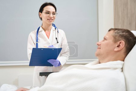 Foto de Primer plano retrato de la sonriente mujer elegante médico está discutiendo con el paciente masculino en la sala de medicina moderna - Imagen libre de derechos