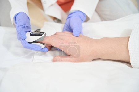Téléchargez les photos : Portrait rapproché des mains du médecin dans les gants mesure la pression artérielle et les niveaux d'oxygène dans le sang à l'hôpital - en image libre de droit