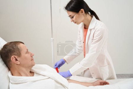 Téléchargez les photos : Portrait de vue latérale de belle infirmière élégante est resserre le garrot sur le bras patient dans le centre de médecine - en image libre de droit