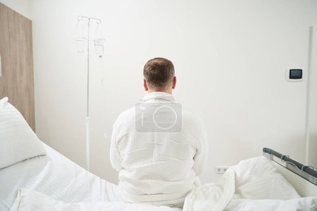 Téléchargez les photos : Portrait de l'homme non reconnu assis sur le lit médical de l'hôpital - en image libre de droit