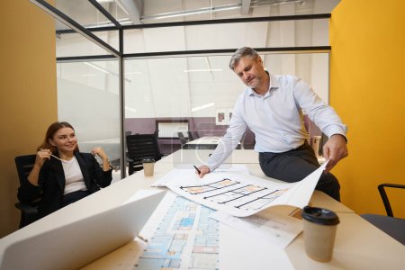 Foto de Hombre de pie cerca de la mesa, mirando los planos arquitectónicos y discutir con la señora en la oficina - Imagen libre de derechos