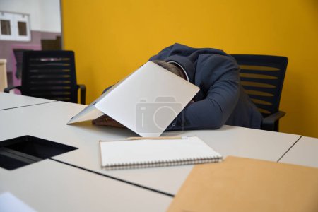 Téléchargez les photos : L'homme assis sur la chaise s'est endormi à la table après s'être couvert d'un ordinateur portable dans le centre d'affaires - en image libre de droit