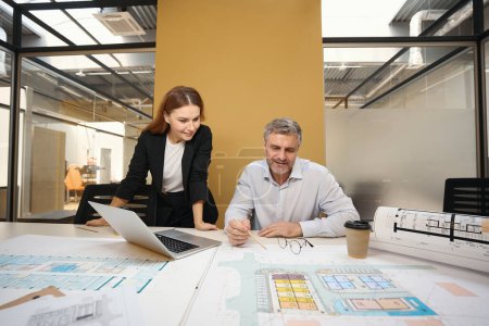 Téléchargez les photos : Homme et femme debout près de la table, regardant les plans architecturaux et discutant - en image libre de droit
