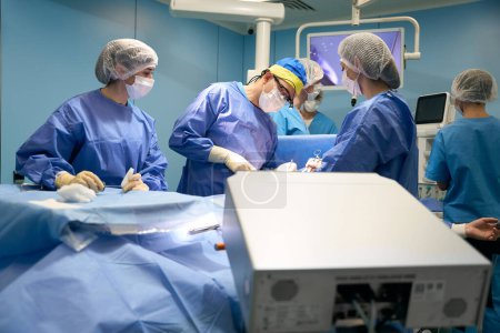 Foto de Cirujano opera al paciente en un quirófano estéril, compañeros asistentes, un anestesiólogo trabaja con él - Imagen libre de derechos