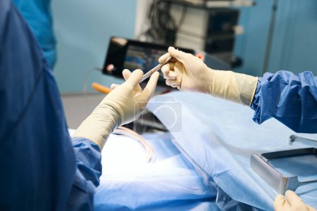 Foto de Médico en quirófano pasando instrumento quirúrgico a asistente colega, personas en uniforme quirúrgico - Imagen libre de derechos