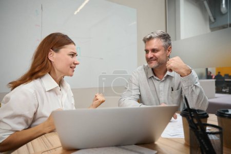 Foto de Mujer sentada en la mesa cerca de la computadora portátil, hombre con ropa de oficina sentado cerca y escuchando - Imagen libre de derechos