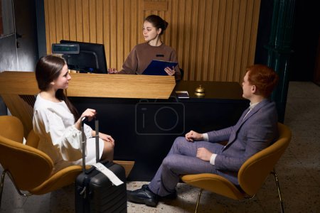 Photo for Young man and woman check into a modern hotel, the staff registers them at the reception - Royalty Free Image