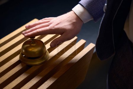Foto de El hombre utiliza una campana para llamar al personal en la recepción, una campana de metal se fija en un panel de madera - Imagen libre de derechos