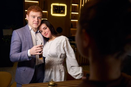 Téléchargez les photos : Jeune couple dans un hôtel moderne, un homme reçoit une clé de chambre - en image libre de droit