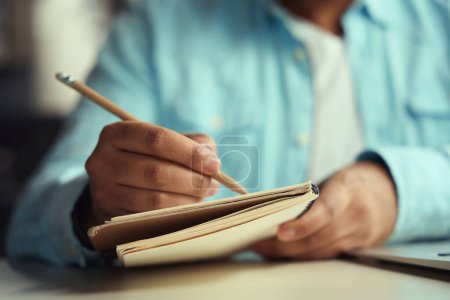 Téléchargez les photos : Homme assis sur une chaise à table et écrivant dans un journal avec un crayon dans le centre d'affaires - en image libre de droit