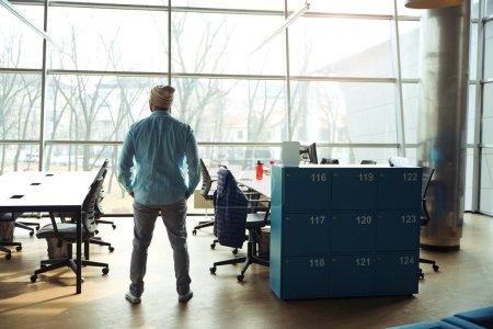 Téléchargez les photos : Homme professionnel en chemise bleue debout dans le bureau près du placard, prêt pour le travail - en image libre de droit