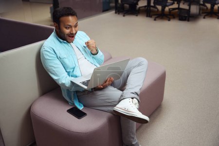 Téléchargez les photos : Homme reposant sur la chaise et se réjouit au travail sur ordinateur portable dans le centre d'affaires - en image libre de droit