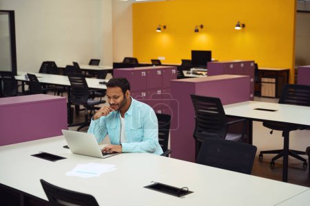 Téléchargez les photos : Homme assis sur une chaise à table et regardant dans l'ordinateur au travail. Concept de travail en coworking - en image libre de droit