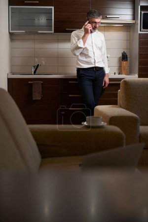 Téléchargez les photos : Homme adulte en tenue de travail debout dans la chambre d'hôtel, parlant avec le client au téléphone, travaillant - en image libre de droit
